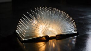 Livro aberto com páginas de vidro sobre uma mesa preta, com luz dourada saindo entre as páginas